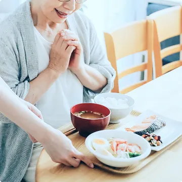 温かい食事が提供され、喜びで手を合わせる高齢の女性の笑顔。